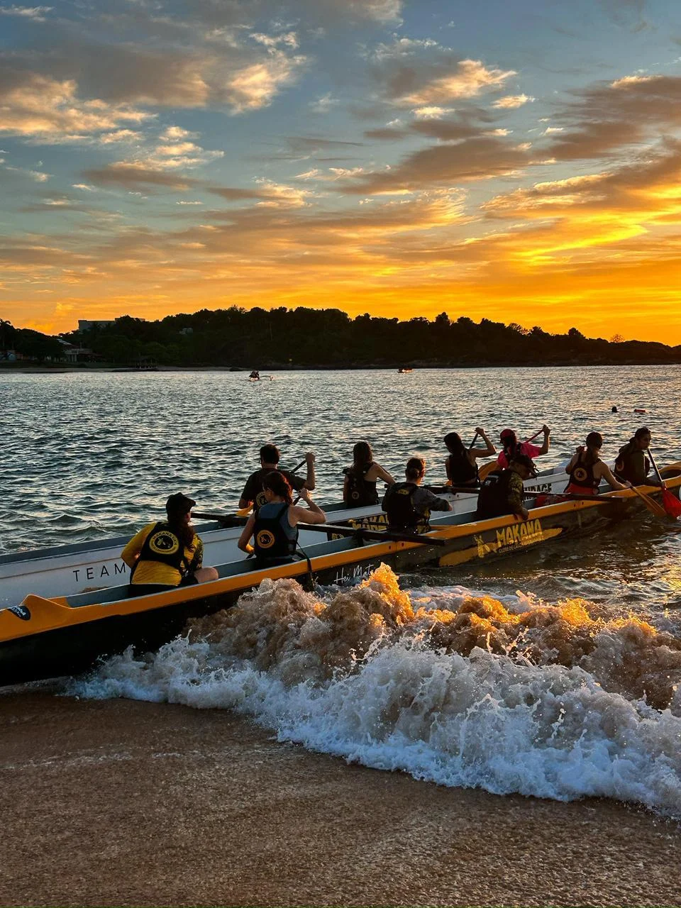 Canoas entrando no mar entre as ondas no fim da tarde