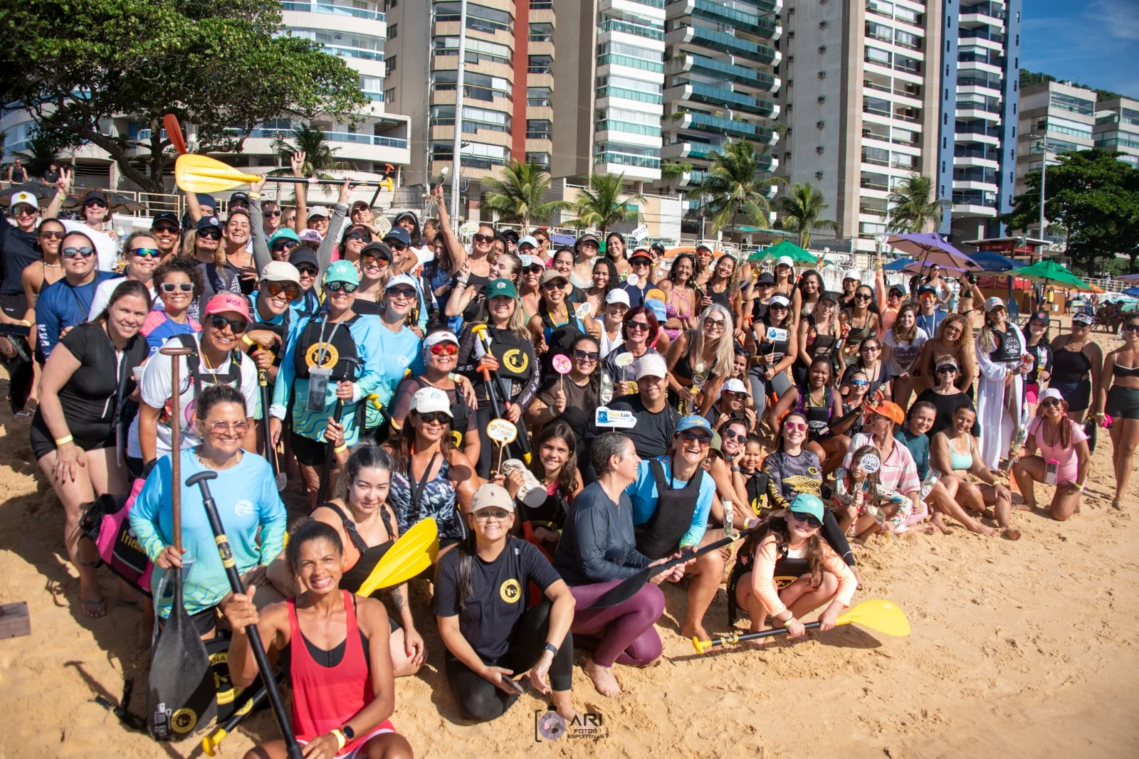 Grupo de remadoras e remadores reunidos na praia com os remos erguidos após a remada