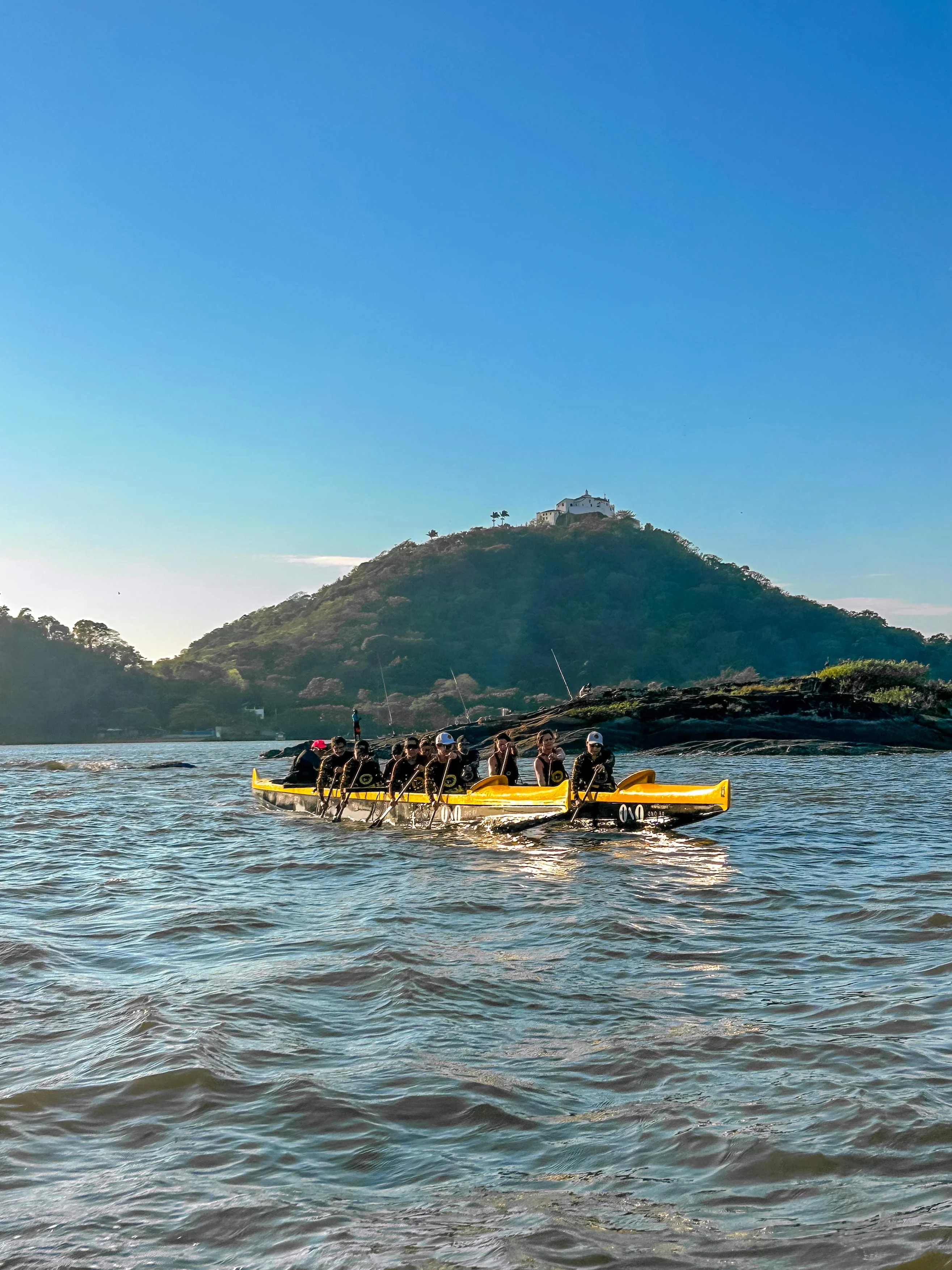 Canoa havaiana amarela remando com o Convento da Penha ao fundo
